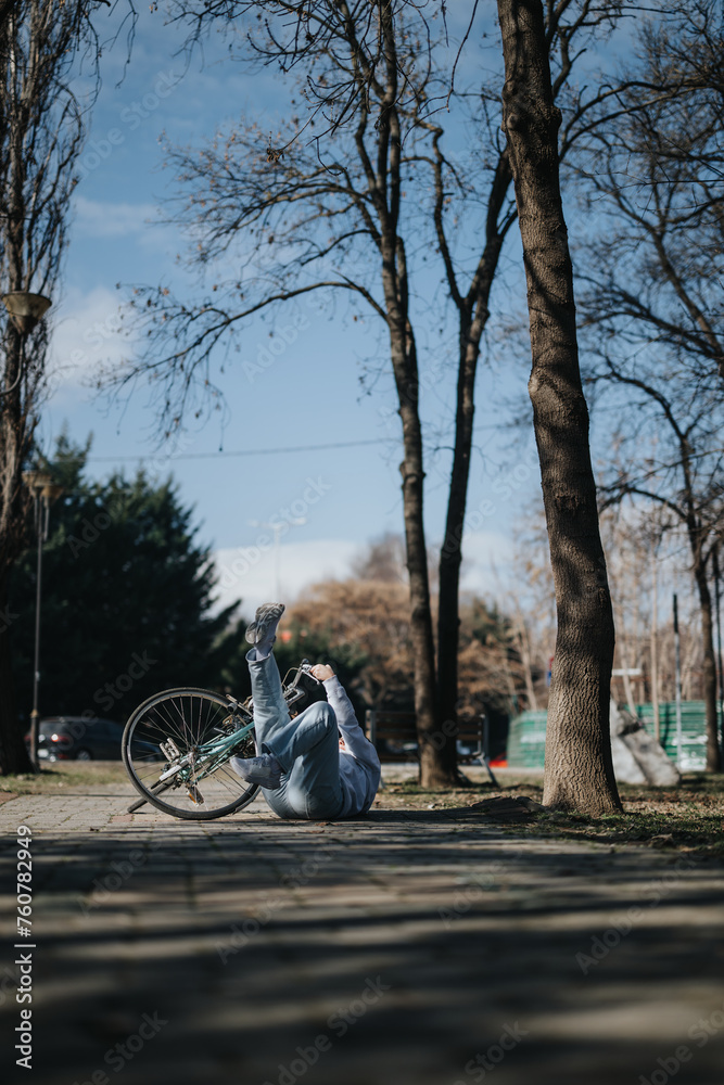 Photo capturing an unanticipated moment as a woman falls off her bike in a serene park setting, surrounded by bare trees and a clear sky.