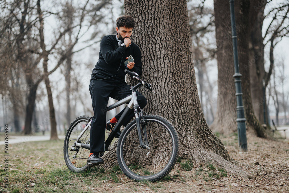 An active male cyclist resting against a tree while checking his smart phone in a serene park setting, possibly tracking his ride or mapping his route.