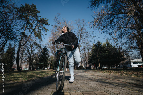 Fototapeta Naklejka Na Ścianę i Meble -  An enthusiastic woman experiences the joy of cycling in a serene park setting under a clear blue sky. A sense of freedom and happiness prevails.