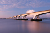 A long bridge over the sea during sunset. Long exposure photo. Landscape during a bright sundown. The sea and the bridge.