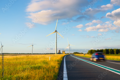 Landscape during sunset with road, field and wind turbines. Windmills for energy production. Green energy in the Netherlands. A beautiful asphalt road with wind power turbines during sunset. © biletskiyevgeniy.com