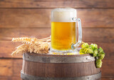 Mug of beer with wheat ears and green hops on wooden barrel