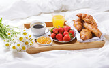 Breakfast in bed. Tray with cup of coffee, croissants, orange juice, fresh fruits and bunch of daisy flowers