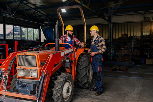 One mechanic sitting in a tractor seat and the other is taking notes.