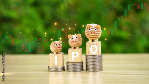 Rows of money coins stacks with IPO word and piggy bank on wooden cube and candlestick charts in the garden background for Initial Public Offering, Increased investment concept, economic concept.