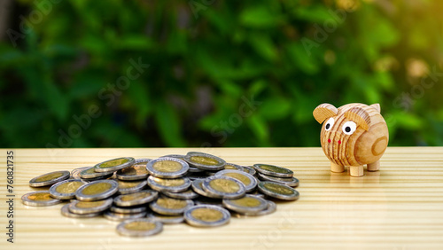 Wooden piggy bank and heap of money coins on a wooden table with a natural background, Financial investment profit in a business concept. Growth money stability, security and saving idea.