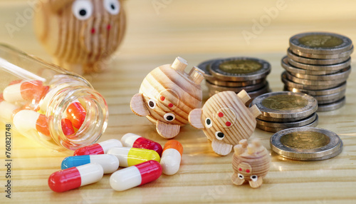 Many miniature wooden piggy bank falls overturned with heap of money coins and colorful medicine pills on table, Money debt problem in medication concept.Crisis of drug high cost in disease treatment.