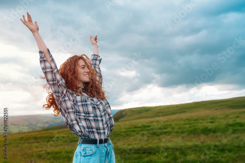 amazing redhead woman raising her hands  reaching the destination and enjoying mountains landscape on the top of mountain at sunset. Enjoy hiking and exploring new places concept