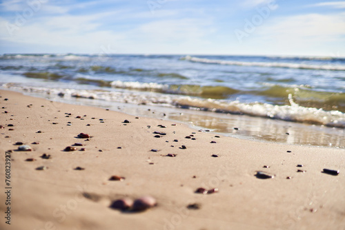 Small smooth pebbles lie on the sand near the shoreline. Selective focus