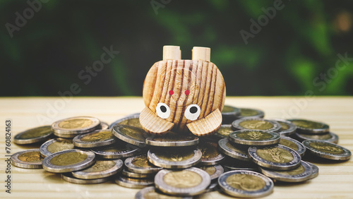 Miniature wooden piggy bank falls overturned on heap of money coins on wood table in blur natural tree, Money debt problem concept.Tax day. Money crisis.