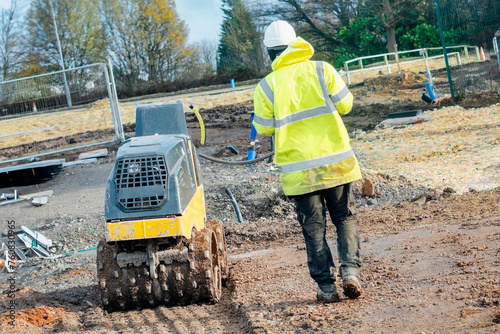 Trench roller with remote control operated by groundworker to compact ground on new housing development building site. Stay away of moving plant photo