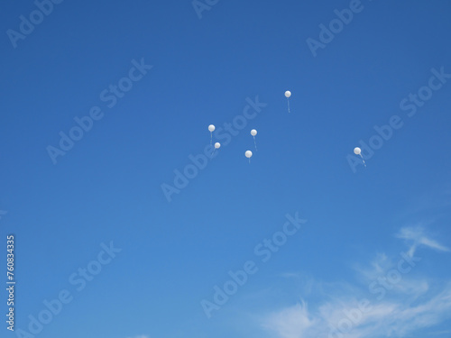 Several white balloons on a blue almost cloudless sky