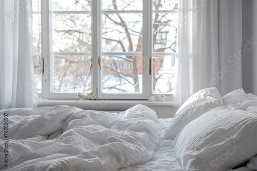 Close up of bed with white bedding against window. The scene is peaceful and serene, with the snow outside creating a sense of calmness © Nico