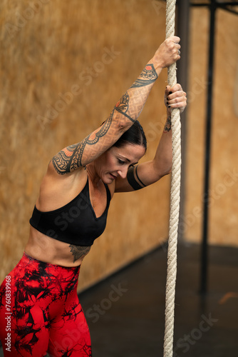 Tired sportive woman climbing a rope in a gym