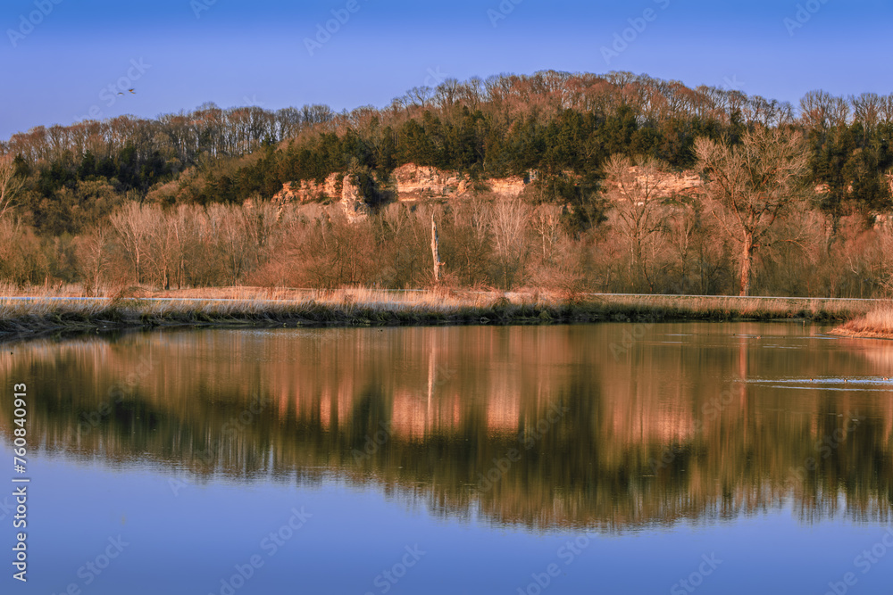 View of Missouri River bluffs  reflecting in calm water at sunsets early in spring; clear sky in background