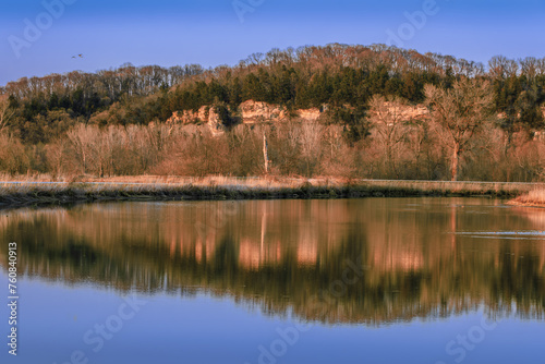 View of Missouri River bluffs reflecting in calm water at sunsets early in spring; clear sky in background