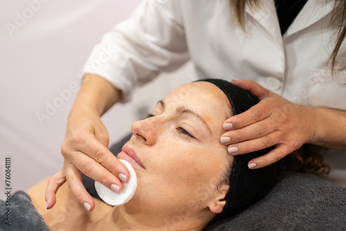 Crop beautician cleaning face of client with skin care cotton pad in beauty salon