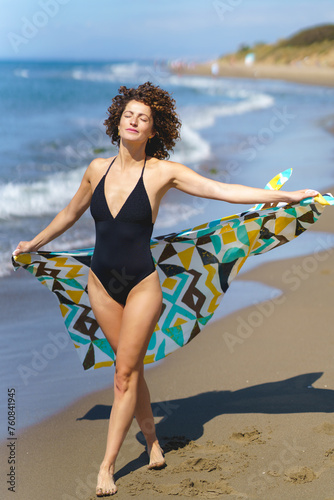 Stylish woman in swimsuit stretching hand on sandy beach