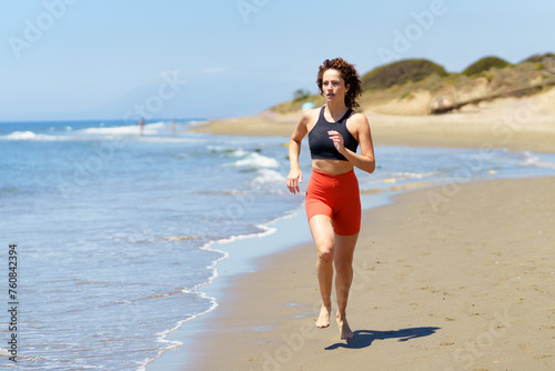 Focused young sportswoman exercising on seashore in daylight