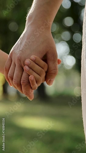 Mother and child holding hands on sunset background. Daughter takes mother's hand in park. Sun flares nature. Concept of family, trust, love and happiness. Vertical video