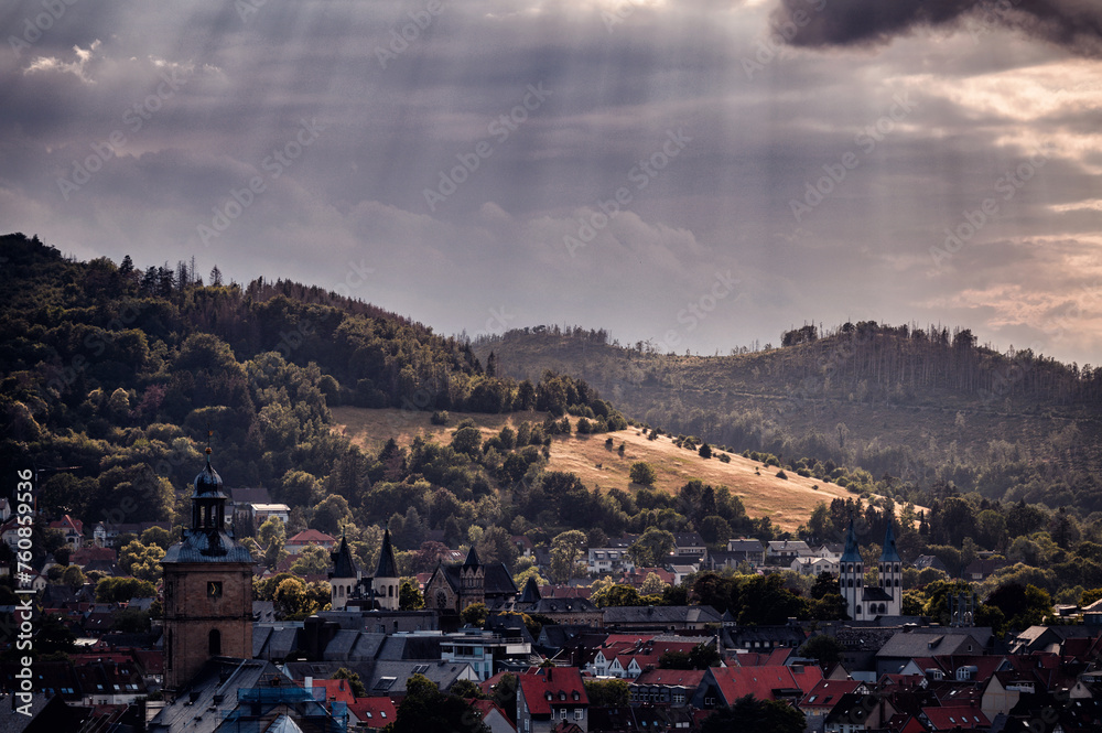 Sunbeams pierce the clouds, illuminating a picturesque town against a backdrop of green hills and historic architecture