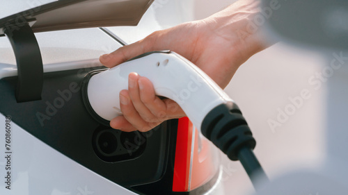 Closeup hand put EV charger to recharge electric car's battery from charging station in city commercial parking lot. Rechargeable EV car for sustainable environmental friendly urban travel. Expedient