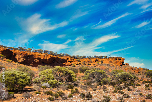 Desert vegetation with salt bush and mulga at the foot of red rocks, near Mount Magnet, mid-west of Western Australia. 
