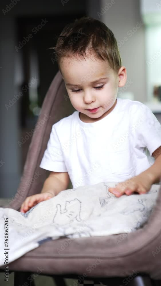 Little boy takes a towel and walks by the kitchen. Kid puts the towel on the chair and smiles to camera. Vertical video. Little boy takes a towel and walks by the kitchen. Kid puts the towel on the chair and smiles to camera. Vertical video.