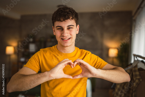 Portrait of one caucasian man 20 years old looking to the camera at home smiling show hand hart gesture