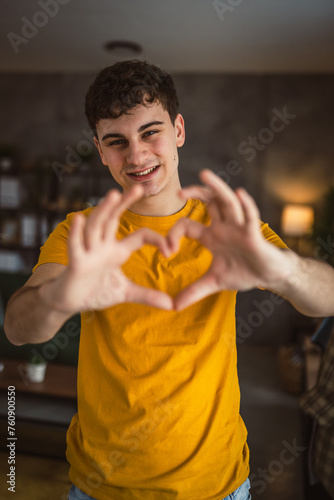 Portrait of one caucasian man 20 years old looking to the camera at home smiling show hand hart gesture