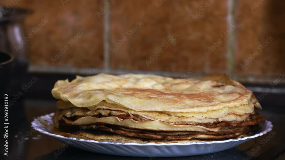 Close-up of a plate of pancakes with another pancake placed on top. Preparation for the celebration of Maslenitsa, background of domestic kitchen with brown tile Close-up of a plate of pancakes with another pancake placed on top. Preparation for the celebration of Maslenitsa, background of domestic kitchen with brown tile
