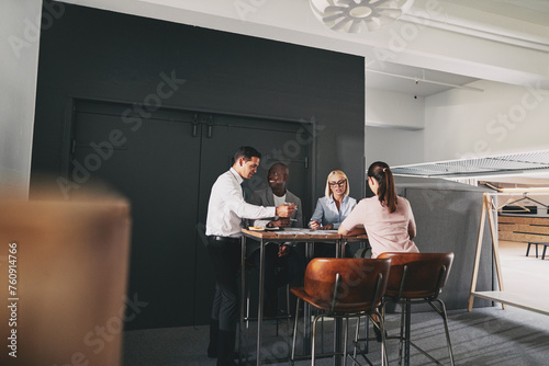 Four mixed race business people sitting at a high table in an office community. They smile at each other and hold a meeting photo