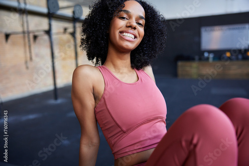 A young black fit woman sits on a floor and smiles at the camera in pink sportswear photo