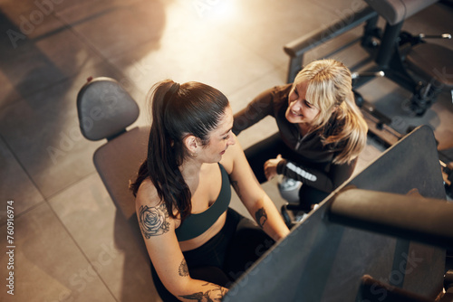 Female trainer a fit young in sportswear smiling during a workout session together on a leg press machine during a exercise class in a gym photo