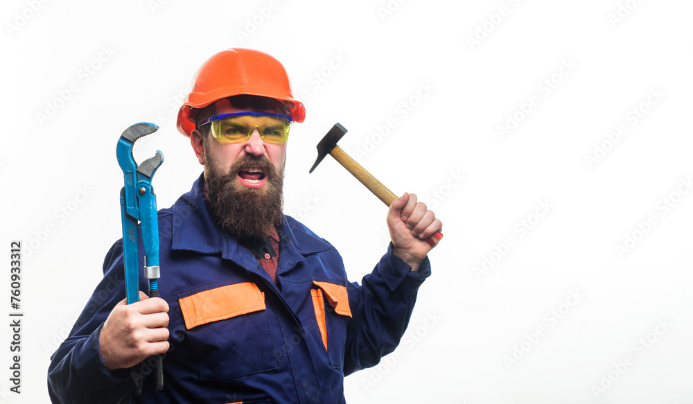 Angry builder in hard hat with adjustable pipe wrench and hammer. Bearded man in construction uniform and protective helmet with adjustable spanner and hammer. Plumber with monkey wrench and hammer. Angry builder in hard hat with adjustable pipe wrench and hammer. Bearded man in construction uniform and protective helmet with adjustable spanner and hammer. Plumber with monkey wrench and hammer.