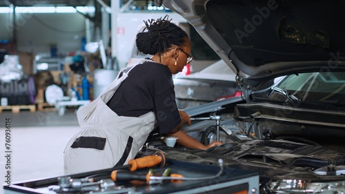 Certified serviceman in garage using torque wrench to tighten bolts inside opened up vehicle, preparing to change oil. Auto repair shop specialist doing checkup on car to prevent problems