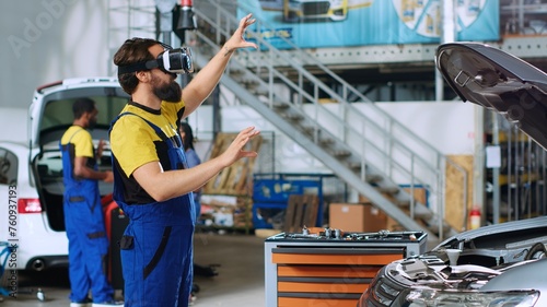 Qualified serviceman in auto repair shop using virtual reality goggles to visualize car components in order to fix them. Expert wearing modern vr headset while working on damaged vehicle