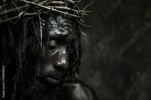 A man with dreadlocks is wearing a crown and looking down