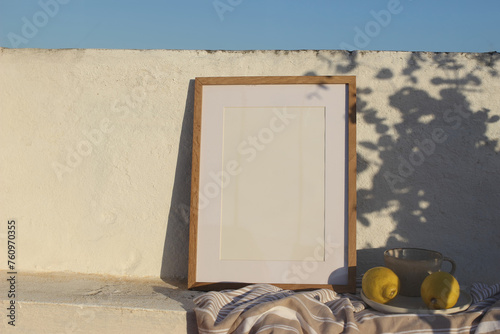 Vertical wooden frame picture mockup against white old textured white wall in sunlight. Fresh yellow lemons fruit, cup of coffee. Mediterranean summer background with light, floral shadows. Blue sky.