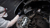 An auto mechanic applies anti-corrosion mastic to the underbody of a car.