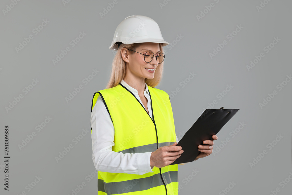 Engineer in hard hat holding clipboard on grey background Engineer in hard hat holding clipboard on grey background