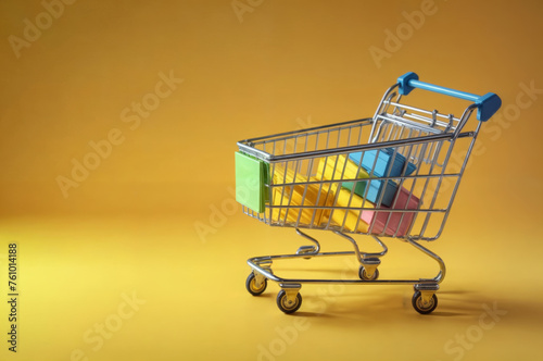 Shopping cart with colorful boxes on a yellow background. Shopping concept.