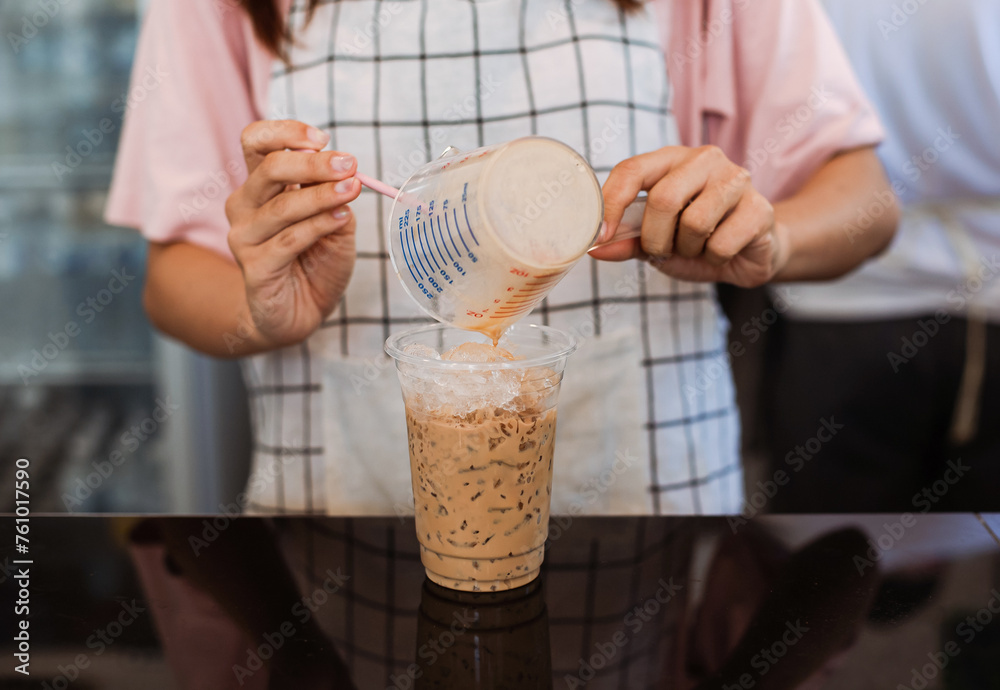 Close-up of young woman preparing coffee By pouring coffee into a glass filled with ice.