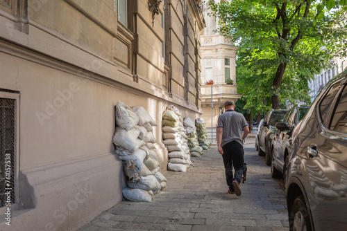 a pedestrian passing beside the sandbags piled up on the windows of historical buildings facing side walk in lviv old city photo