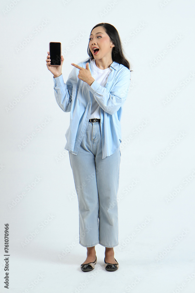 full leght shoot of happy asian indonesian woman holding phone and showing blank screen on isolated background full leght shoot of happy asian indonesian woman holding phone and showing blank screen on isolated background