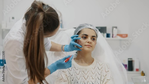 Doctor cosmetologist makes facial markings to woman before cosmetic injection