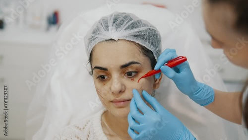 A cosmetologist makes marks on a girls face for injection