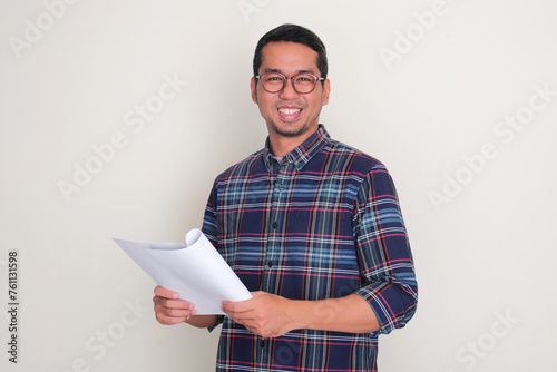 Adult Asian man smiling confident while holding paper document photo