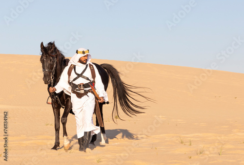 Saudi man walking in a desert with his horse by his side
