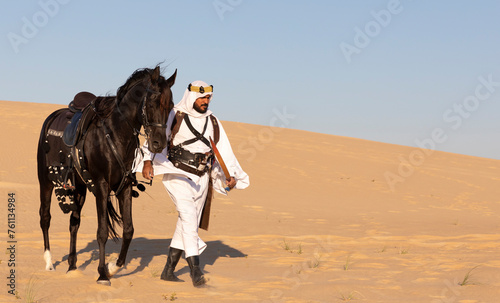 Saudi man walking in a desert with his horse by his side